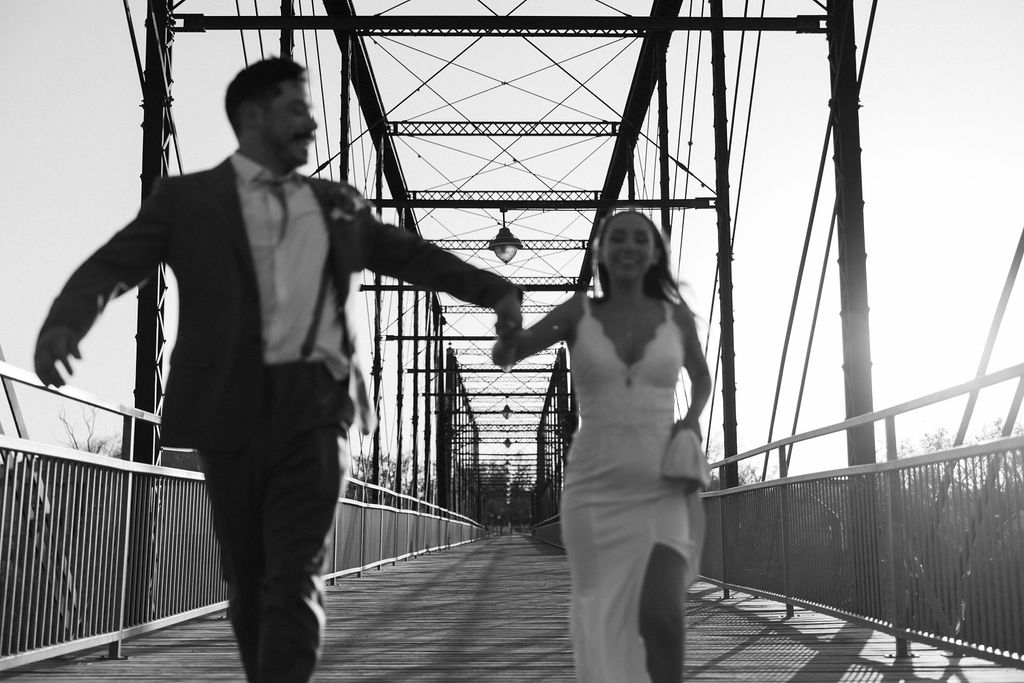 A couple joyfully running hand in hand across a bridge during sunset, showcasing a romantic and candid moment during their destination wedding