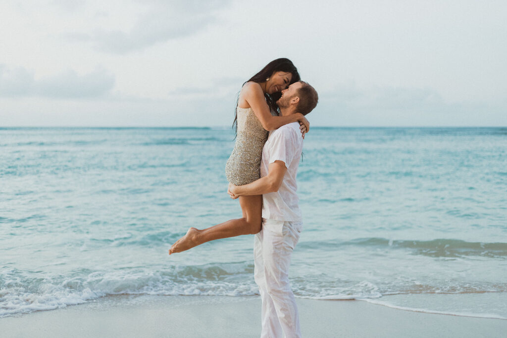 A couple embracing on a beach, with the ocean in the background and a romantic atmosphere.