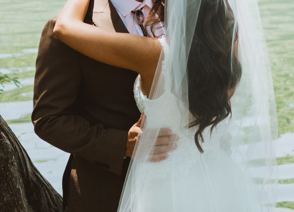 close up of groom holding his bride by her waist by the river in the Texas Hill Country