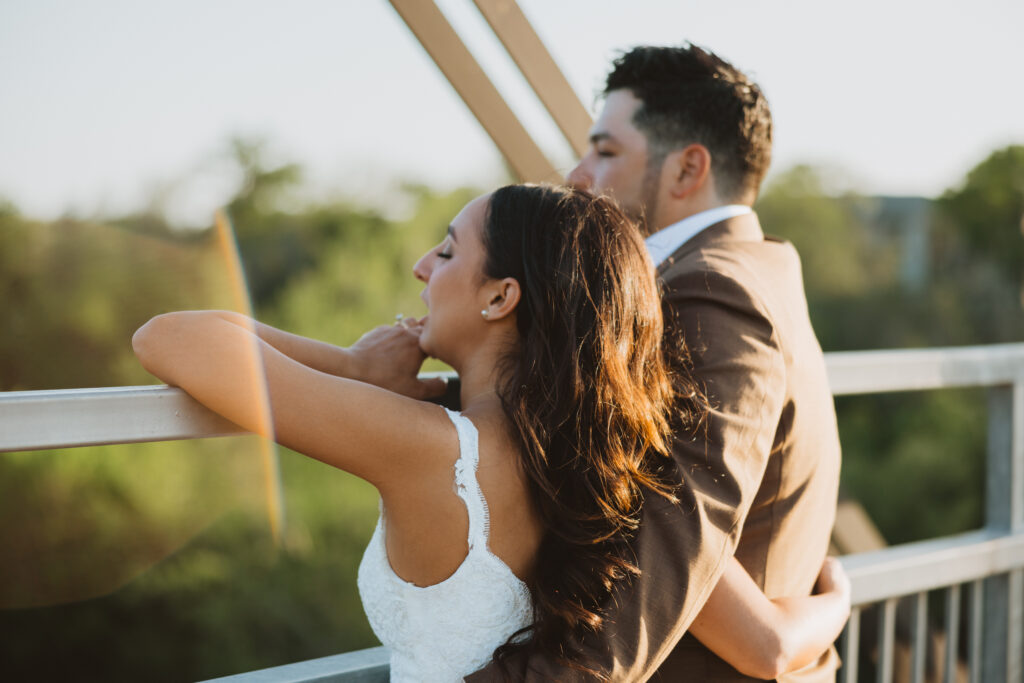 bride and groom waving over a bridge