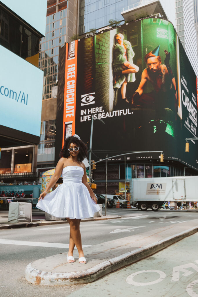 Bride in a short white dress, veil, and sunglasses poses confidently in the middle of Times Square, New York City, surrounded by bold billboards and urban energy.