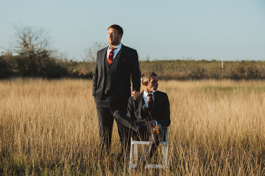Two grooms sitting in a field looking stoic on their wedding day