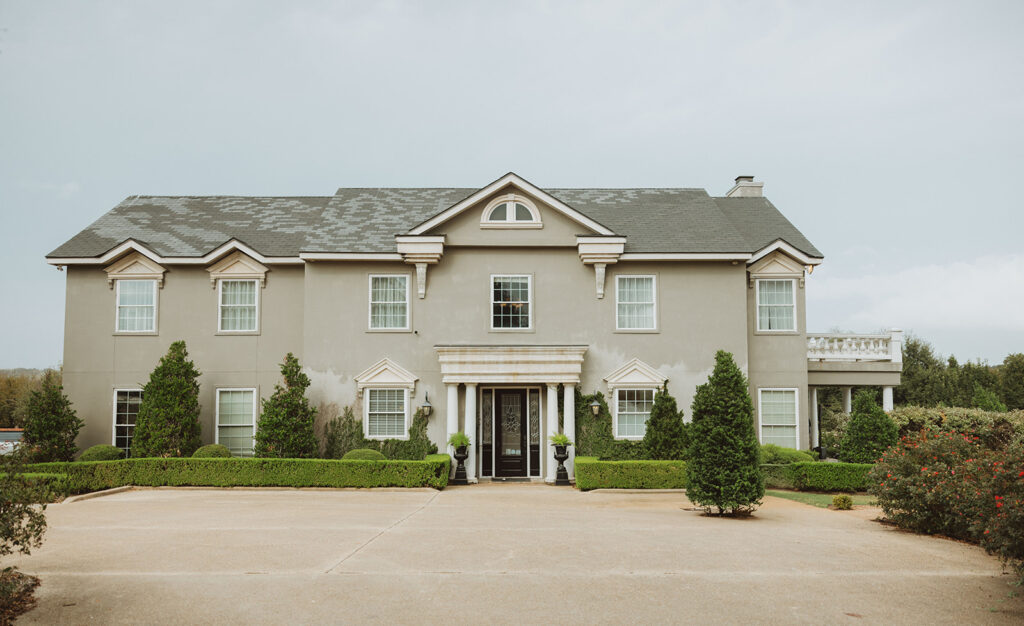 Front view of a stately two-story estate with symmetrical architecture, large windows, and manicured landscaping, featuring a central columned entrance.