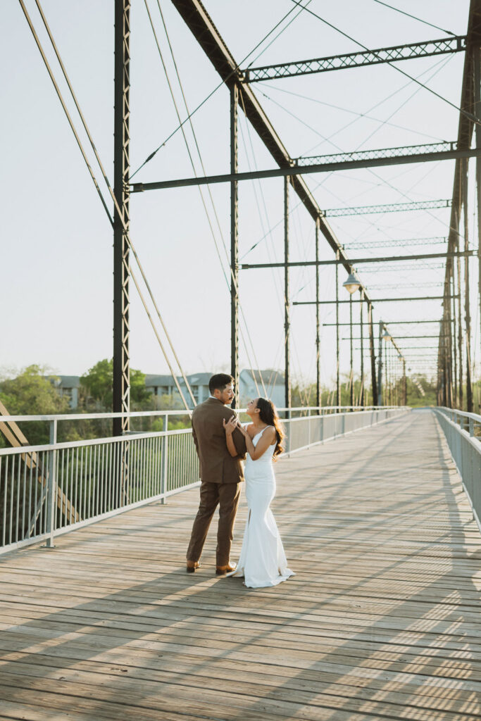Bride and Groom stand in the center of a bridge during sunset