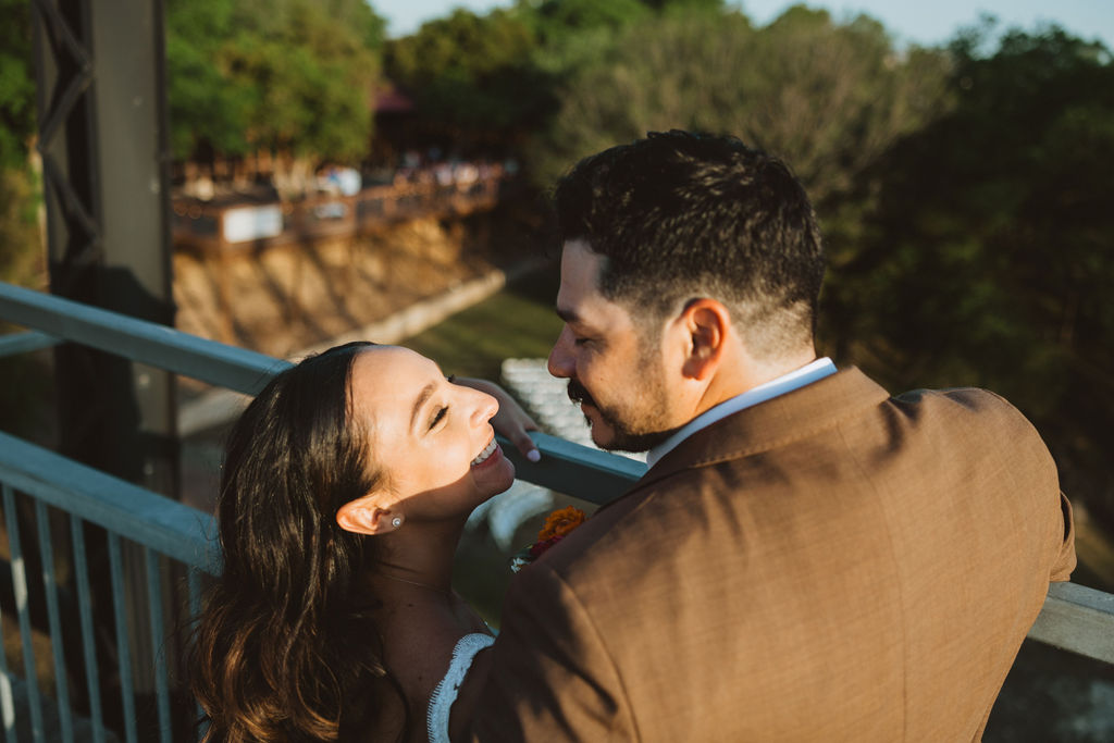 bride and groom smile at each other while family admires form below the bridge