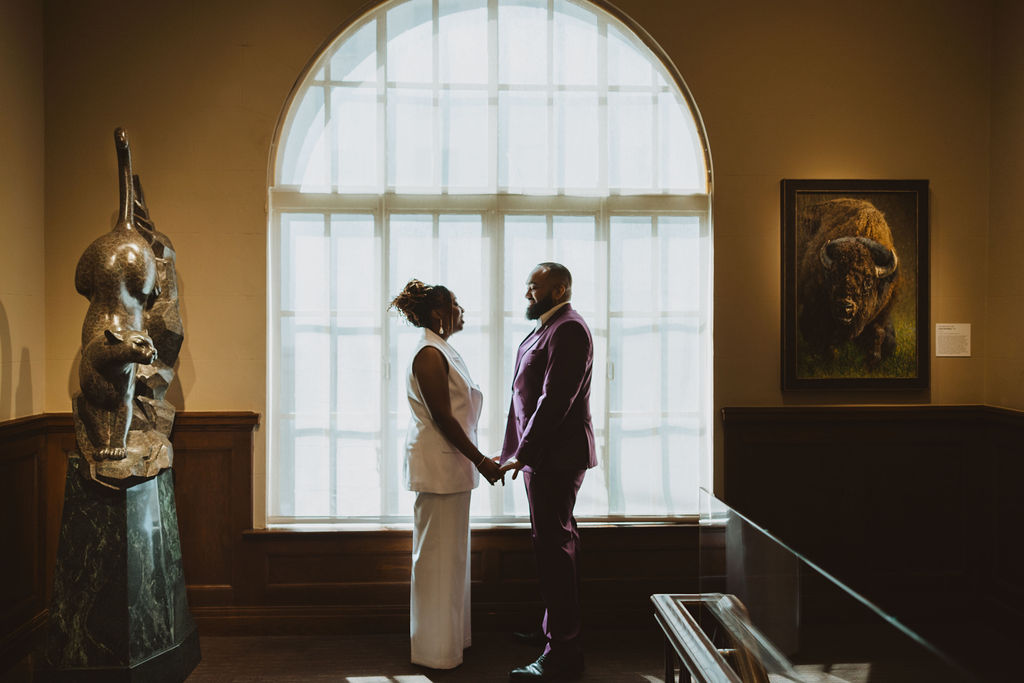A bride and groom standing in a high contrast environment with a backlight arch window