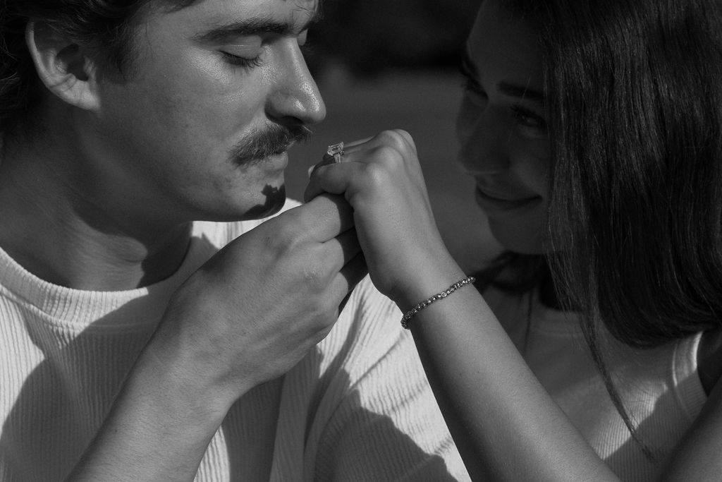 a black and white photo of a man kissing a woman's hand with an engagement ring