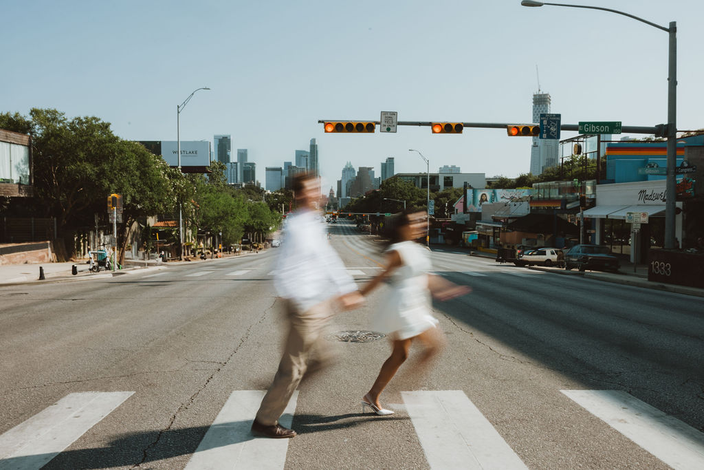 A man and woman walk across a cross walk ono Gibson St in Austin, TX
