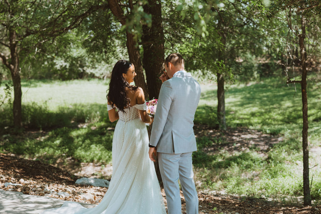 A bride and groom share a private moment surrounded by greenery and warm sunlight