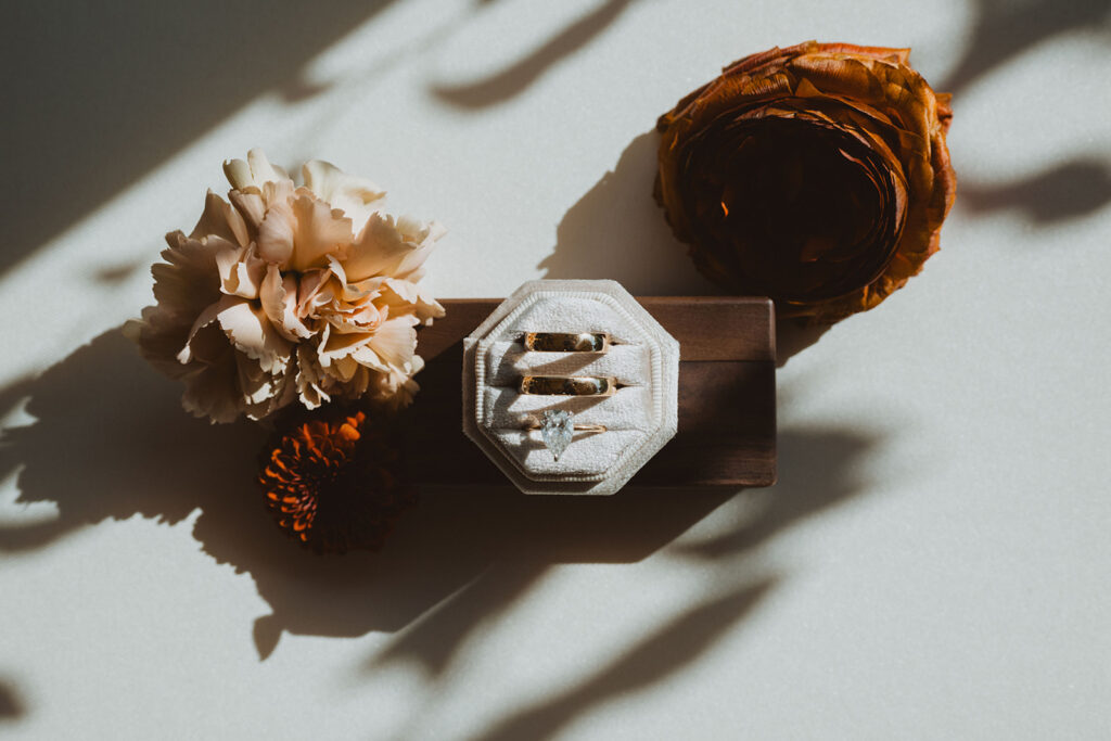 a moody photo of wedding rings and florals with shadows and soft light