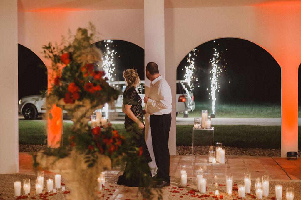 a bride and groom in a breezeway with candles, red uplighting and roses surrounding them
