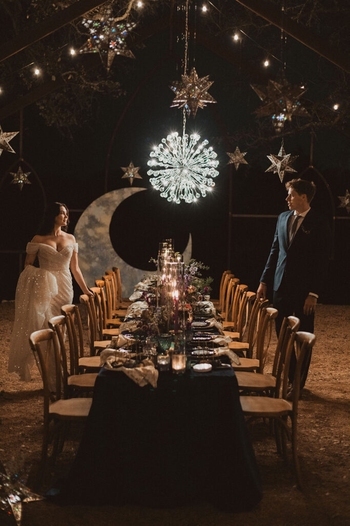 A bride and groom standing on opposite sides of their dinner table in a celestial decorated space