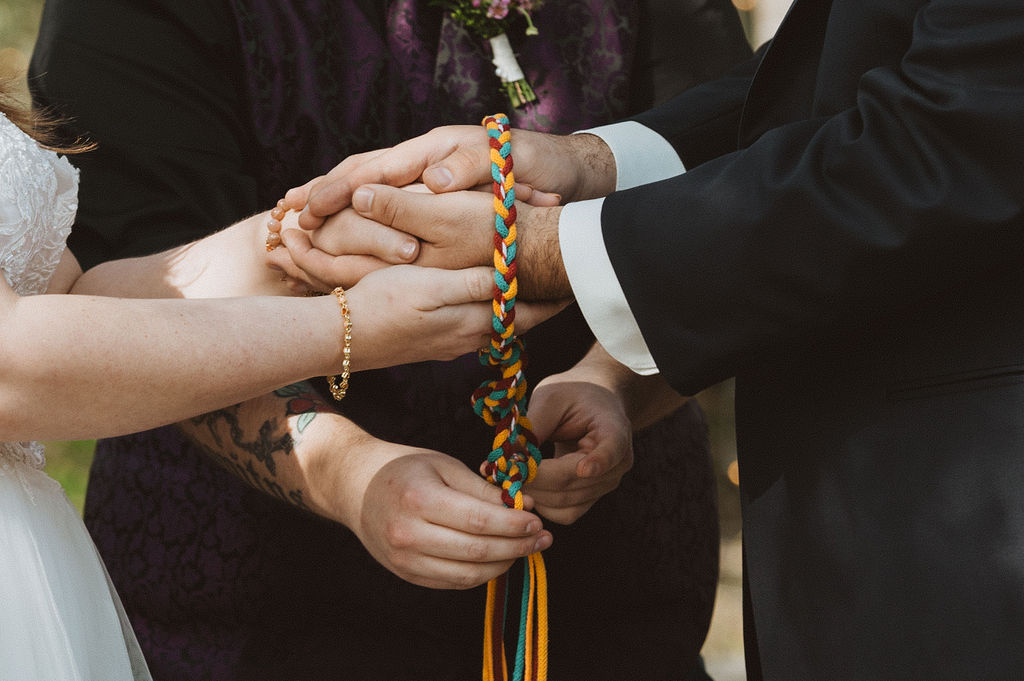bride and groom hold hands tied by a unity knot during their ceremony