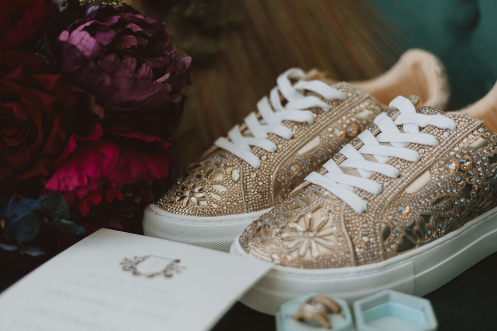 Fashion-forward bridal details featuring gold crystal sneakers, luxury wedding rings, and deep red florals.