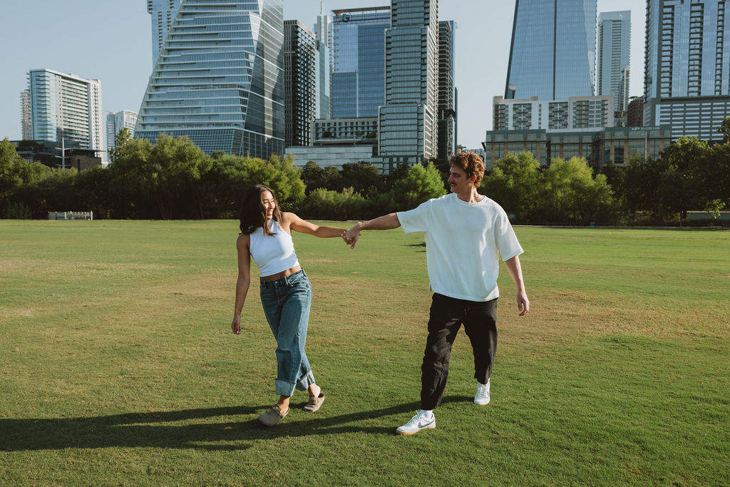 A couple holding hands walking with the Austin skyline as the backdrop